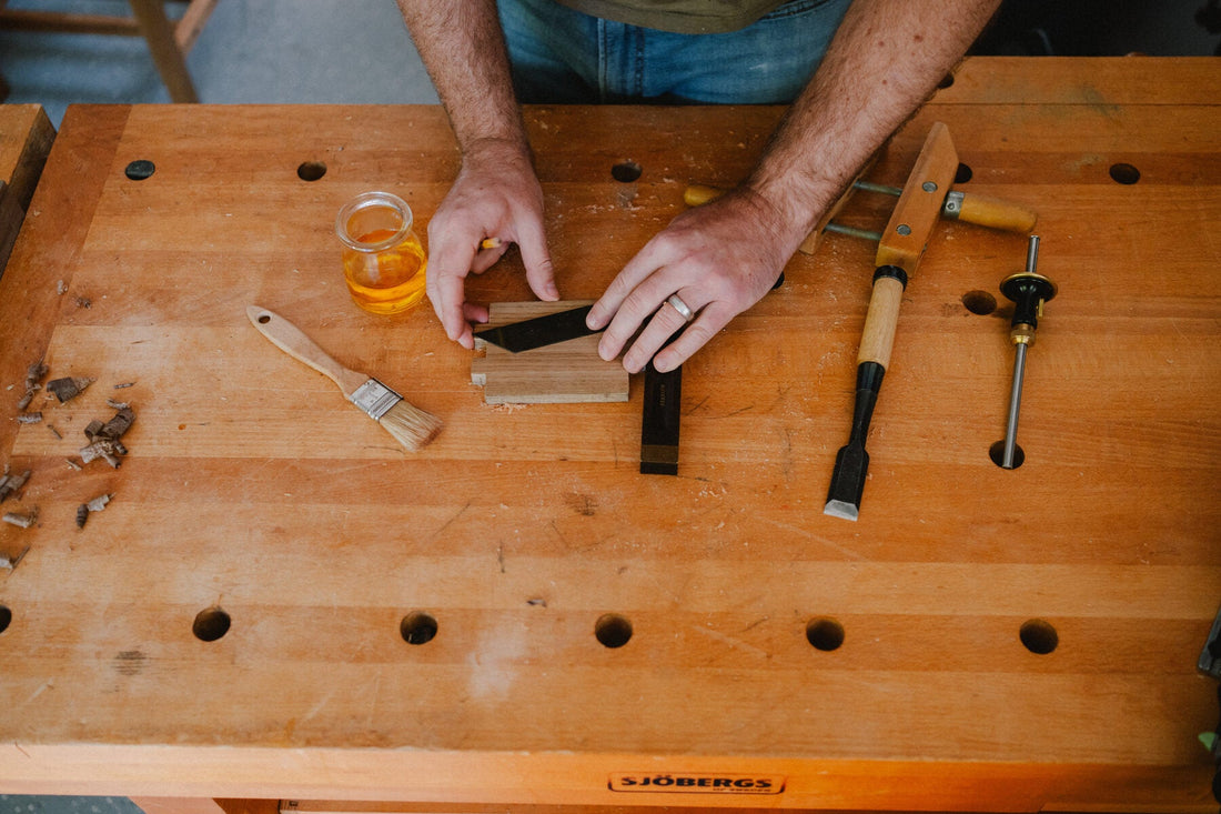 A jar of shellac on a maple workbench beside chisels and a brush