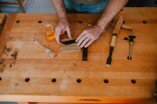 A jar of shellac on a maple workbench beside chisels and a brush