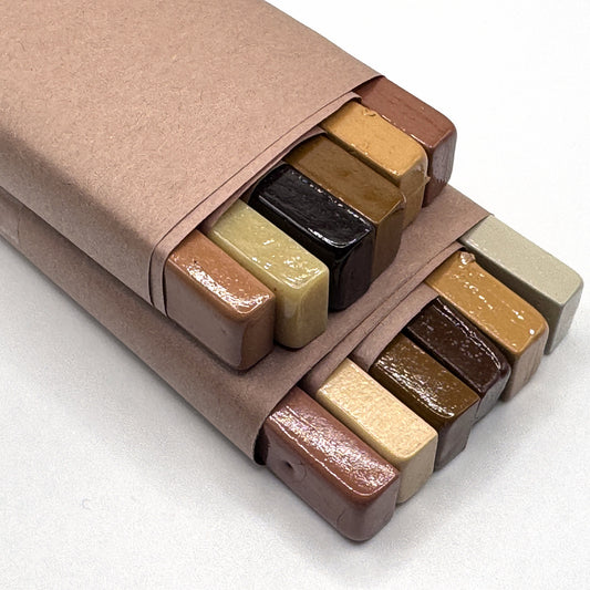 The Wood Tones Dozen — twelve full-size Merit burn-in sticks in their kraft box, the natural wood-tone range from parchment and blonde through cedar and teak to coffee